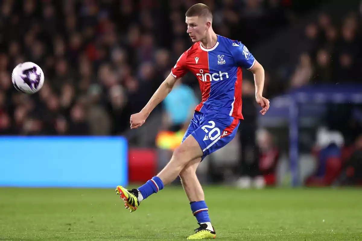 Soccer player in a blue and red uniform kicking a ball in a stadium during a match Soccer player in a blue and red uniform kicking a ball in a stadium during a match