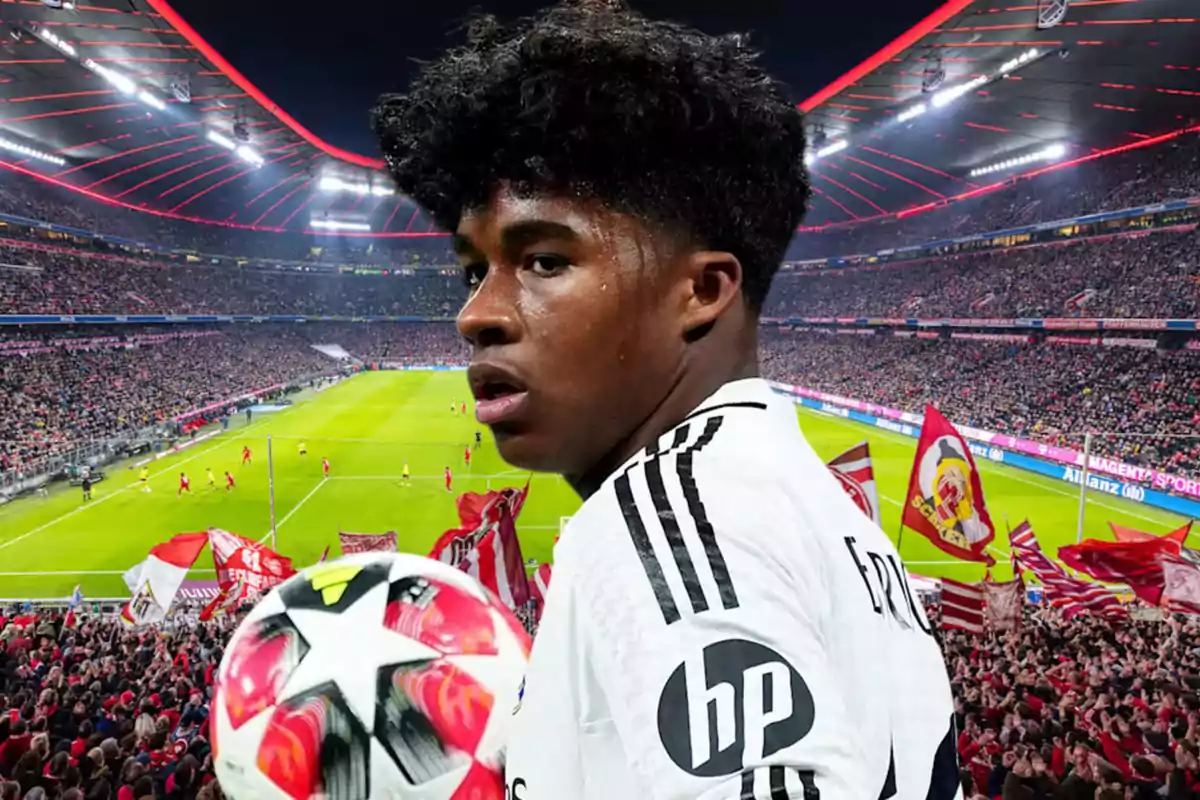 A player in a white uniform holds a ball in front of a stadium full of fans and flags during a soccer match.