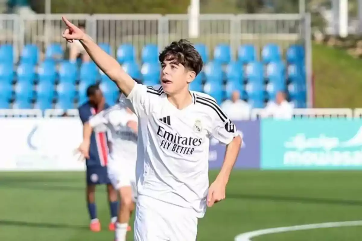 Young player in a white uniform celebrating a goal on a soccer field, pointing his right arm toward the sky Young player in a white uniform celebrating a goal on a soccer field, pointing his right arm toward the sky