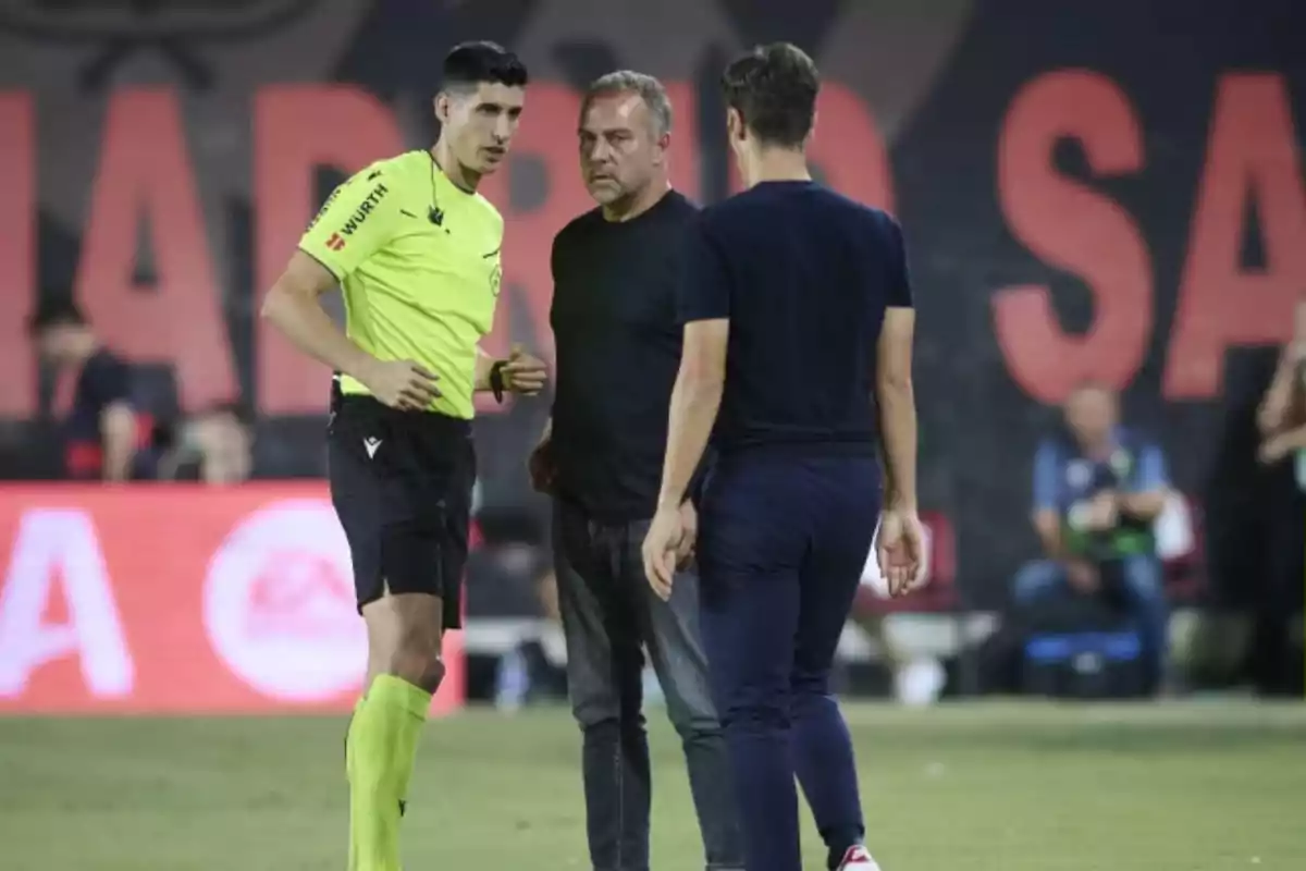 Un árbitro de fútbol conversa con dos personas en el campo durante un partido Un árbitro de fútbol conversa con dos personas en el campo durante un partido