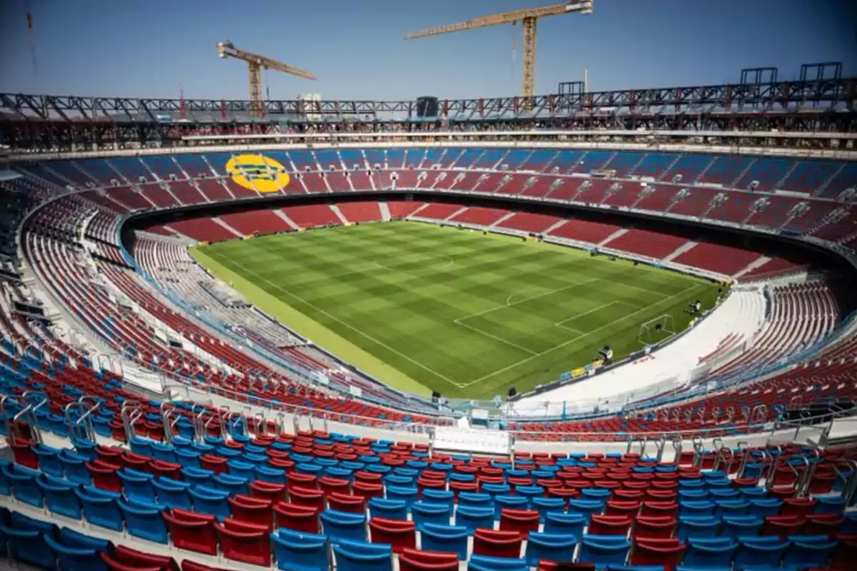 Empty soccer stadium with colorful stands and construction cranes in the background Empty soccer stadium with colorful stands and construction cranes in the background
