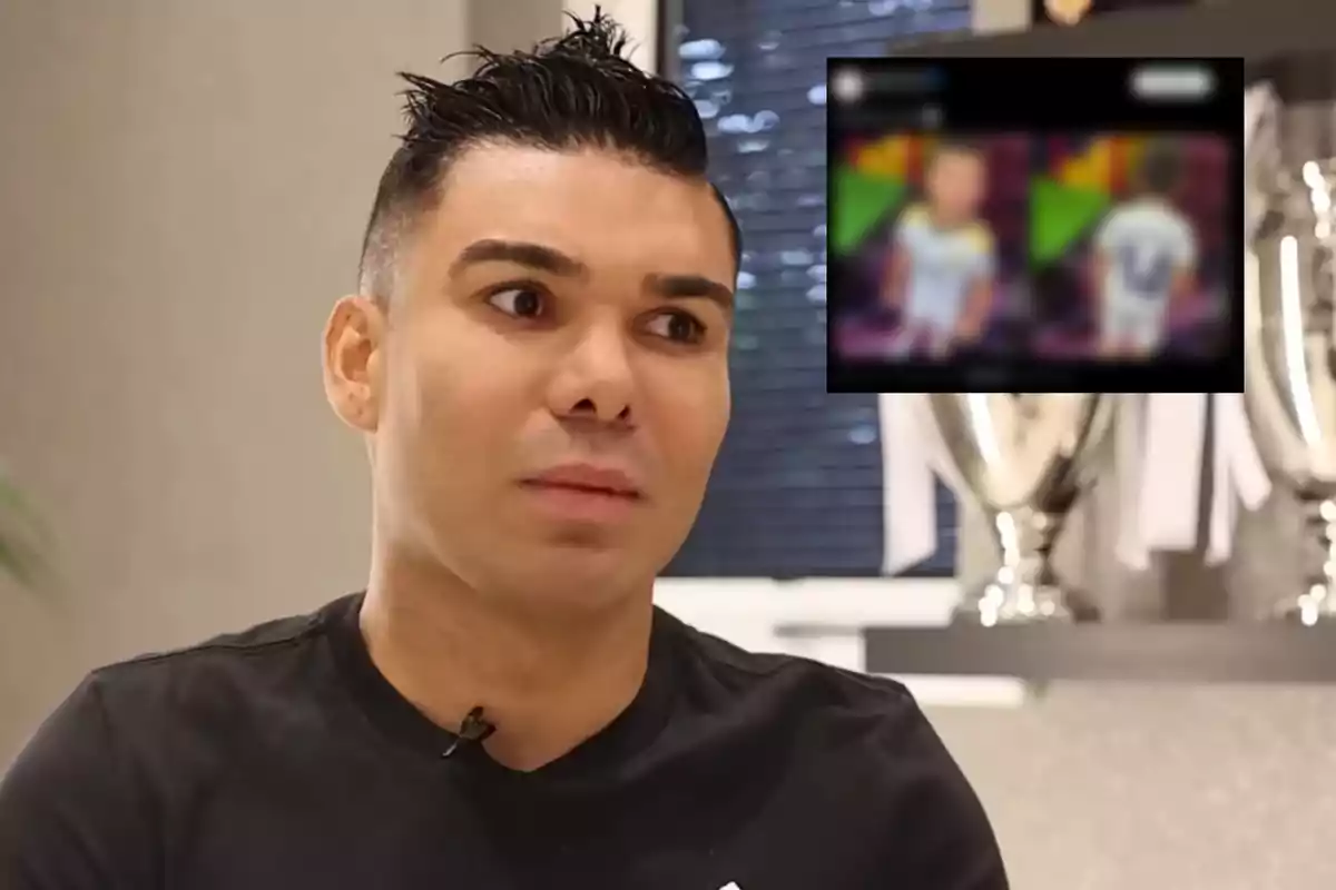 A man with short dark hair looks to the side with a serious expression; in the background, trophies and a blurry screen can be seen.