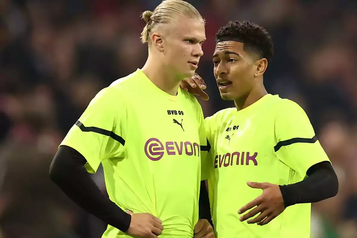 Two Borussia Dortmund players in neon yellow uniforms talk on the field during a match. Two Borussia Dortmund players in neon yellow uniforms talk on the field during a match.