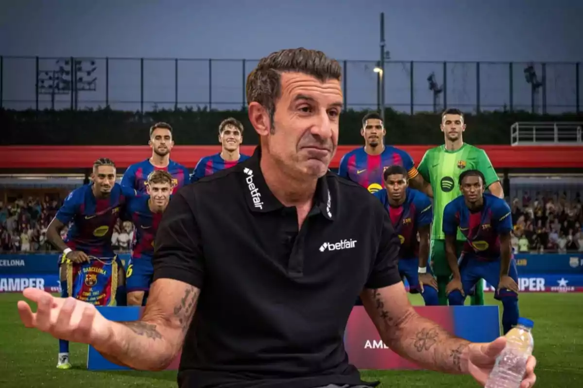 A man wearing a black t-jersey and a doubtful expression is standing in front of a group of players in blue and red uniforms on a soccer field.