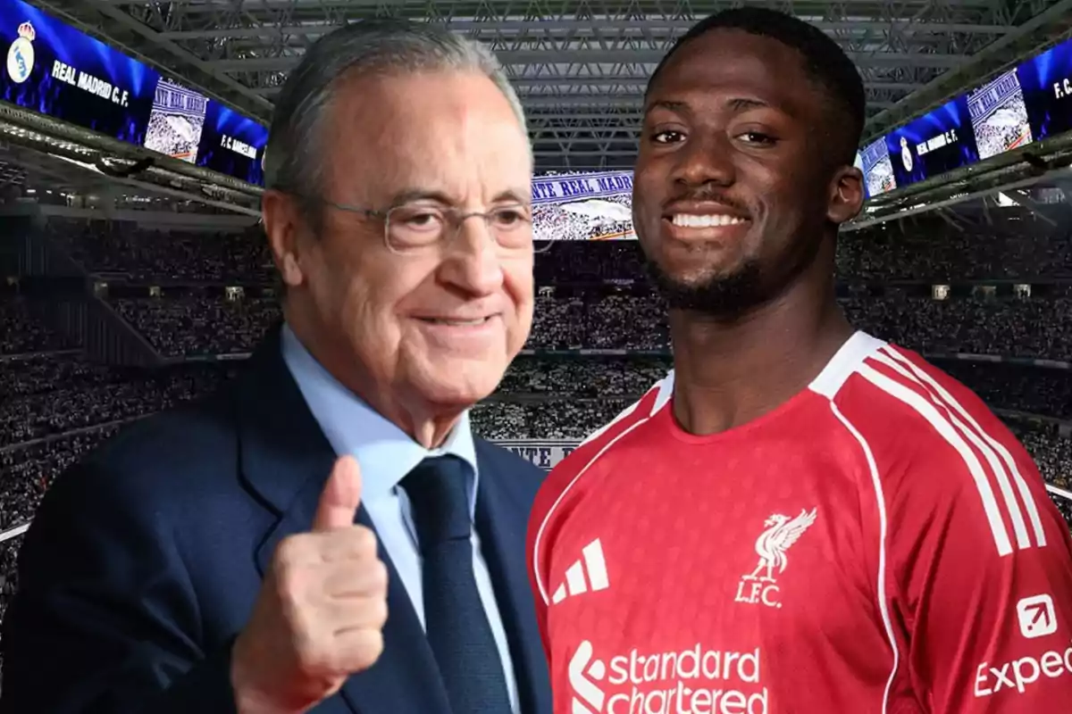 A man in a suit smiles and gives a thumbs up next to a player in a red jersey in a stadium full of spectators.