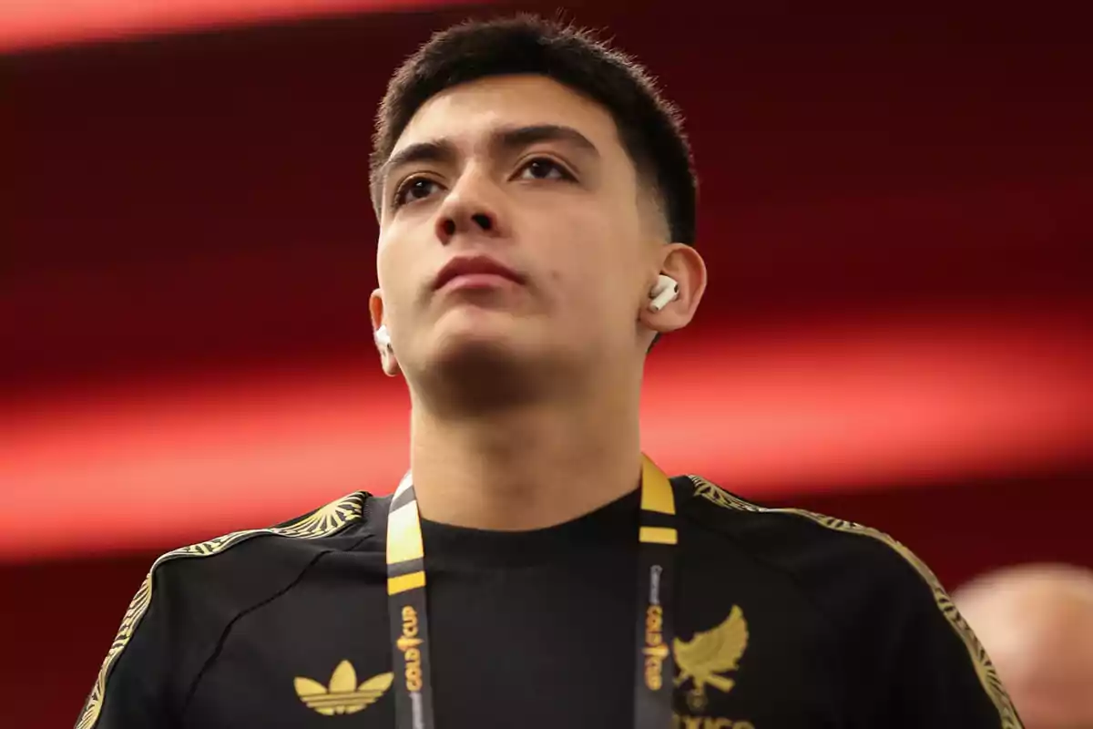Young man with headphones and a black t-jersey with gold details looking up in an indoor setting with a blurred red background Young man with headphones and a black t-jersey with gold details looking up in an indoor setting with a blurred red background