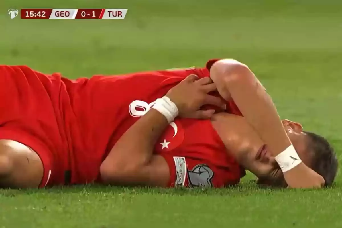 Futbolista con uniforme rojo tirado en el césped sujetándose el pecho y el rostro durante un partido entre Georgia y Turquía