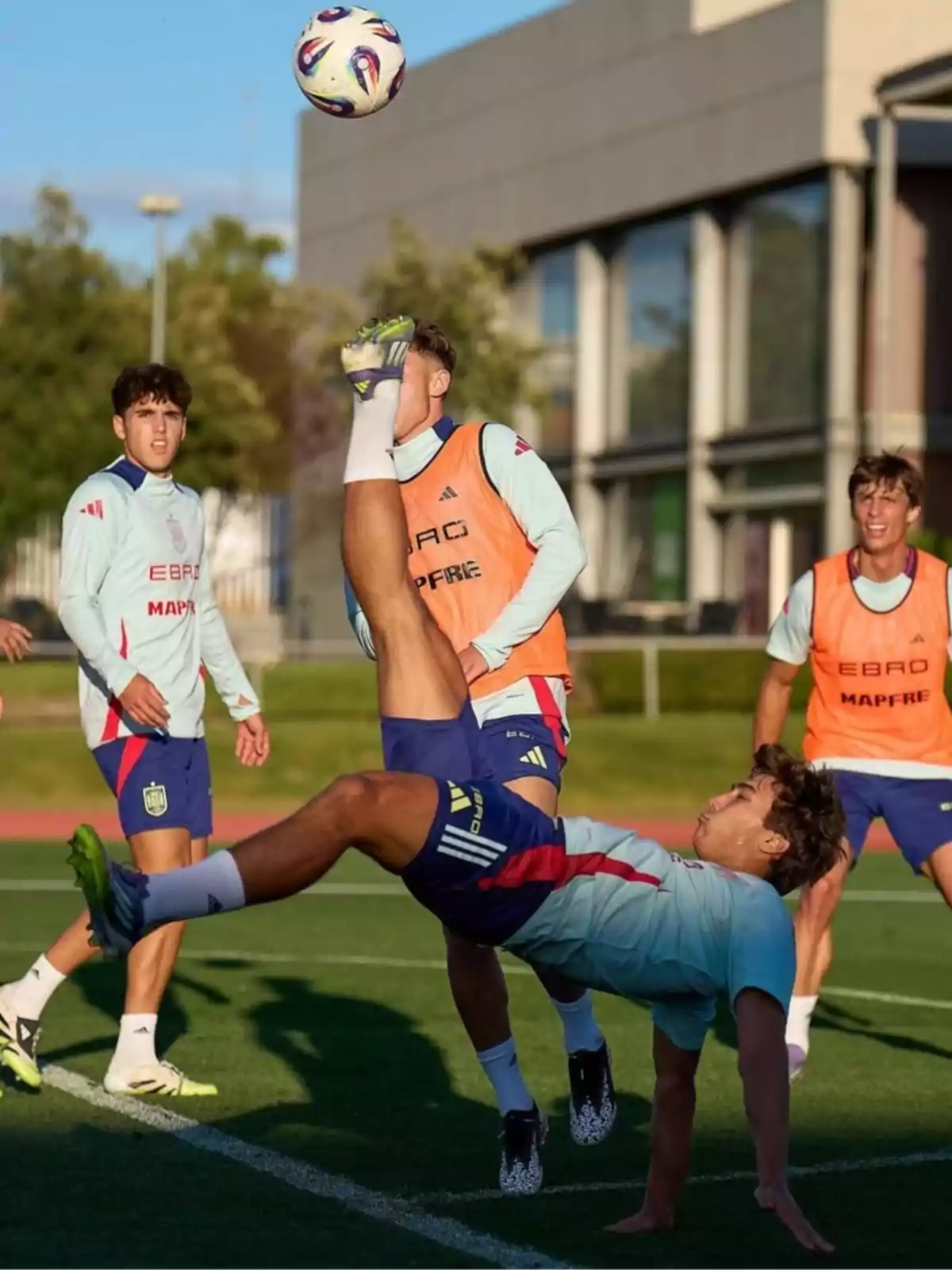 A player performs a bicycle kick during a training session while other teammates watch on the field. A player performs a bicycle kick during a training session while other teammates watch on the field.