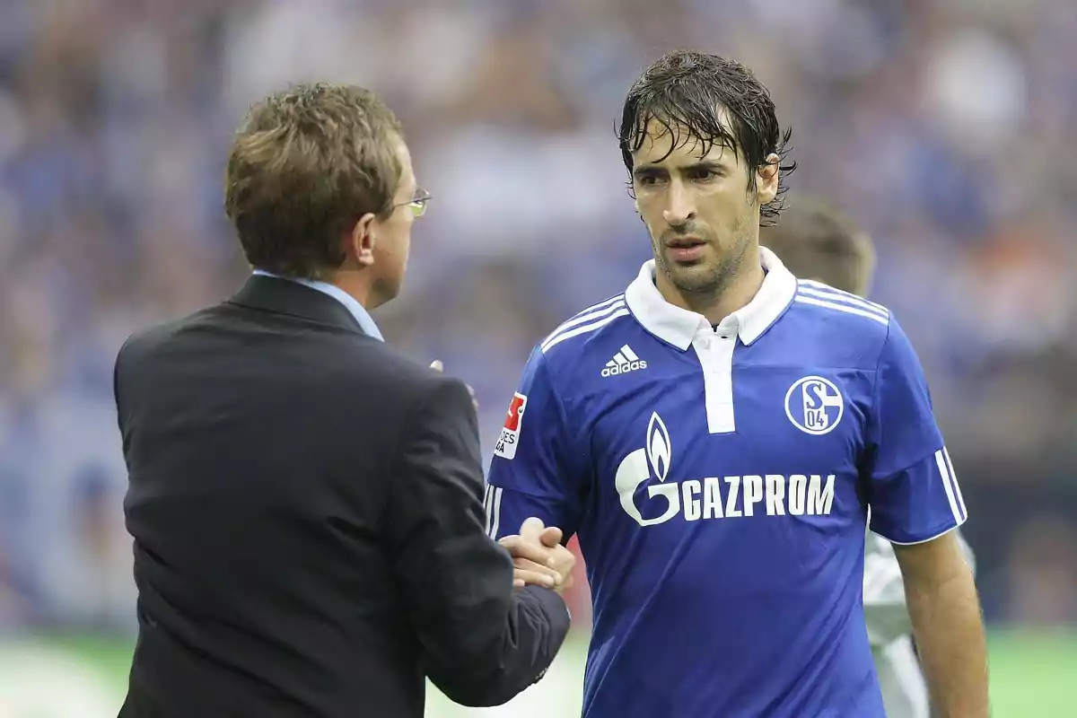 A coach and a Schalke 04 player shake hands on the field during a match. A coach and a Schalke 04 player shake hands on the field during a match.