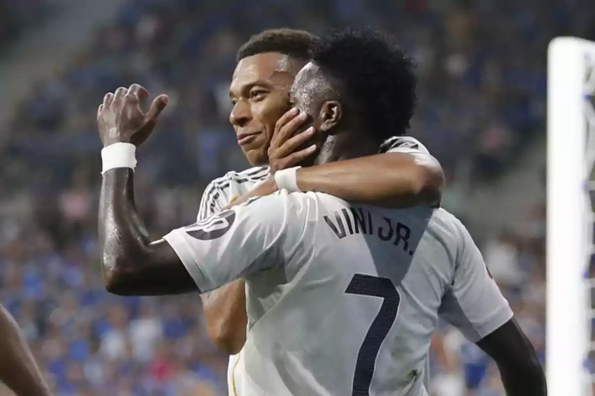 Two players celebrate a goal by hugging on the field; one of them is wearing a jersey with the name Vini Jr. and the number 7. Two players celebrate a goal by hugging on the field; one of them is wearing a jersey with the name Vini Jr. and the number 7.