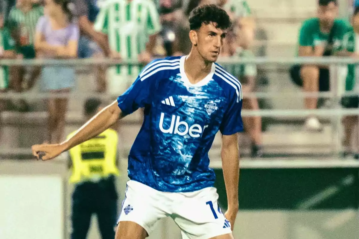 Soccer player in a blue Como team uniform during a match, with spectators in the stands in the background Soccer player in a blue Como team uniform during a match, with spectators in the stands in the background