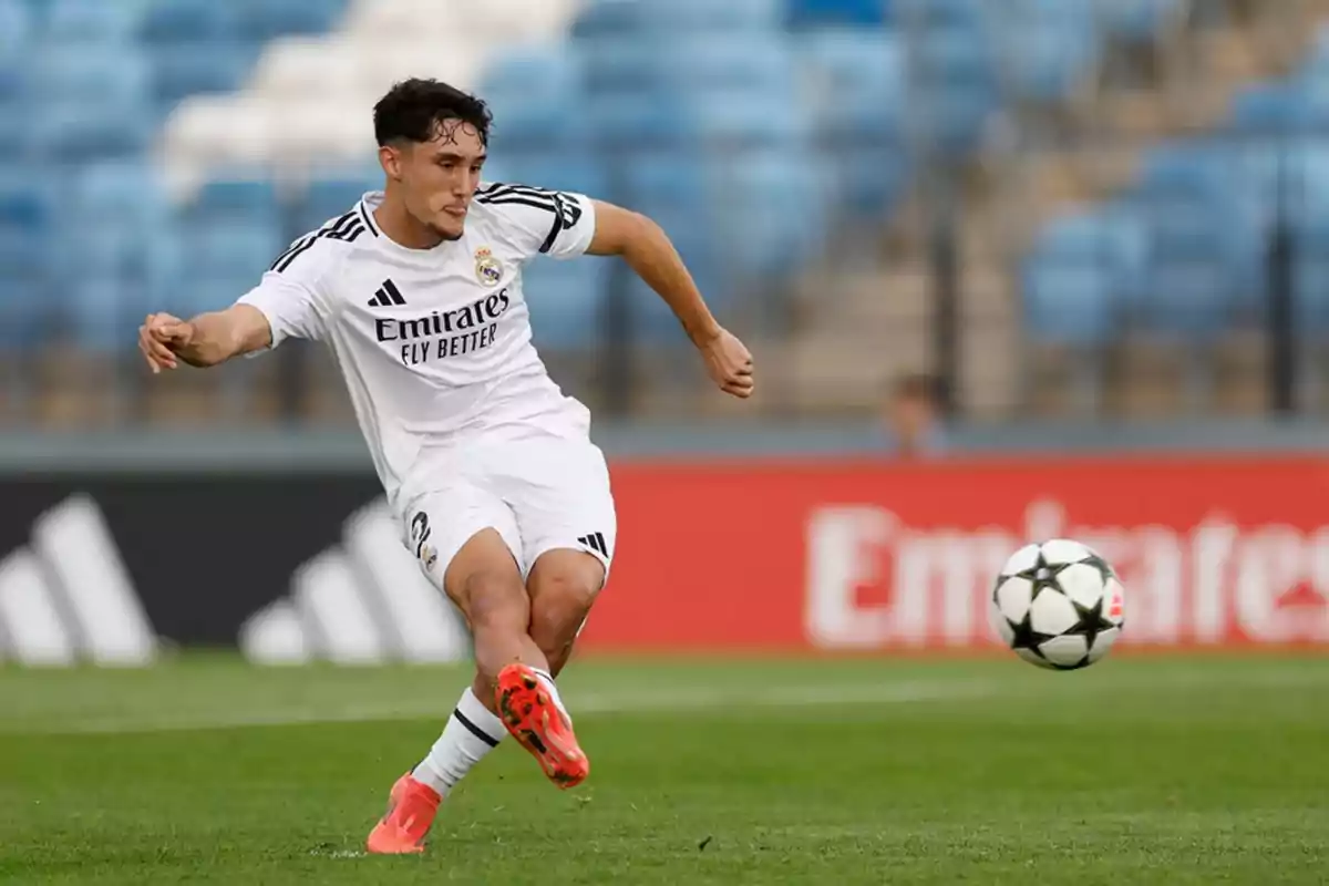 Jugador de fútbol del Real Madrid con uniforme blanco pateando un balón en un estadio Jugador de fútbol del Real Madrid con uniforme blanco pateando un balón en un estadio
