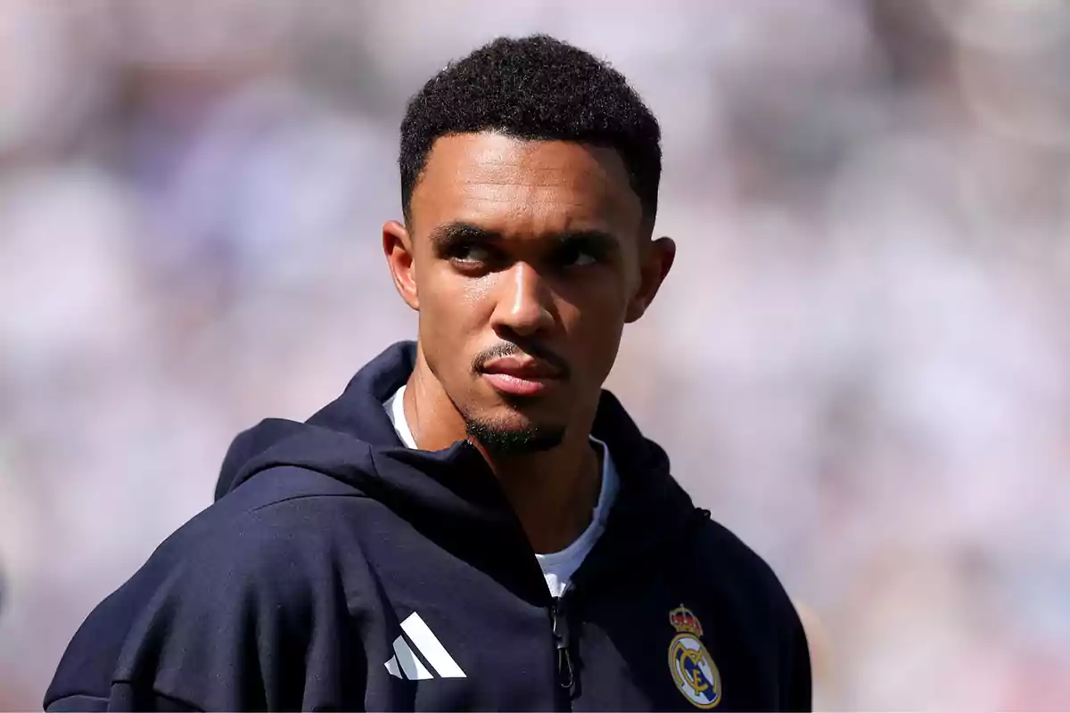 Un futbolista con chaqueta azul marino del Real Madrid mira hacia un lado en un estadio iluminado por la luz del sol Un futbolista con chaqueta azul marino del Real Madrid mira hacia un lado en un estadio iluminado por la luz del sol