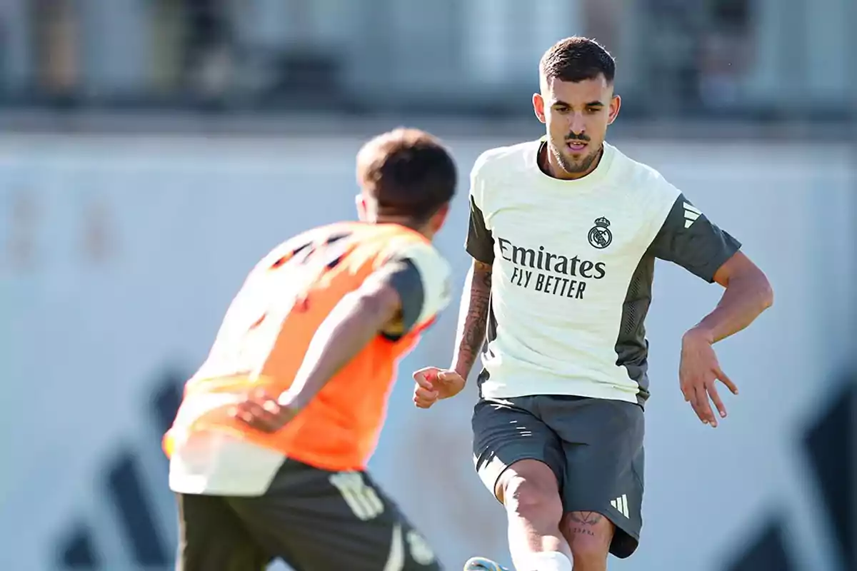 Dos futbolistas entrenando con el uniforme del Real Madrid uno de ellos lleva un peto naranja y el otro está a punto de patear el balón