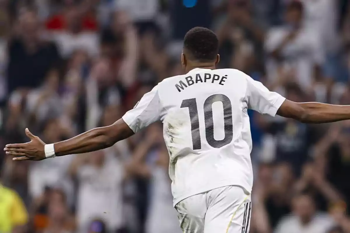 Soccer player wearing the number 10 and the name Mbappé on the jersey celebrating with arms outstretched in a stadium full of fans Soccer player wearing the number 10 and the name Mbappé on the jersey celebrating with arms outstretched in a stadium full of fans