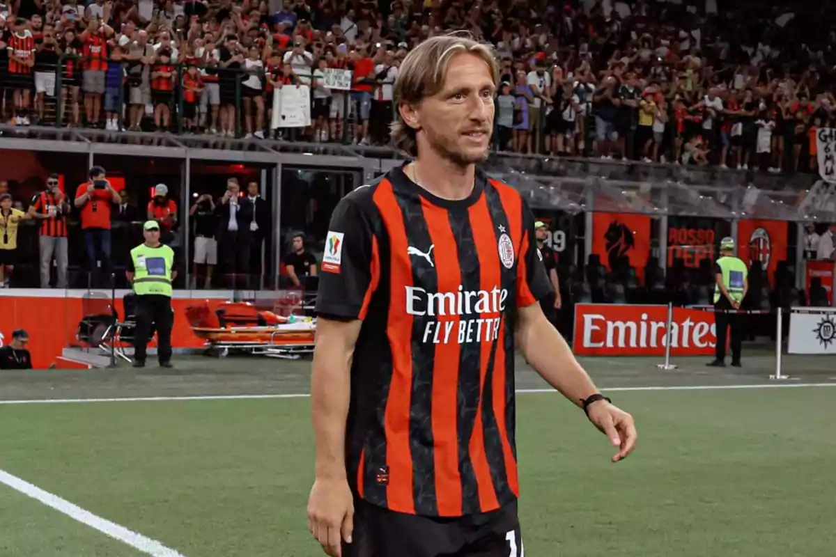 Soccer player wearing an AC Milan uniform on the field during a match with fans in the stands in the background