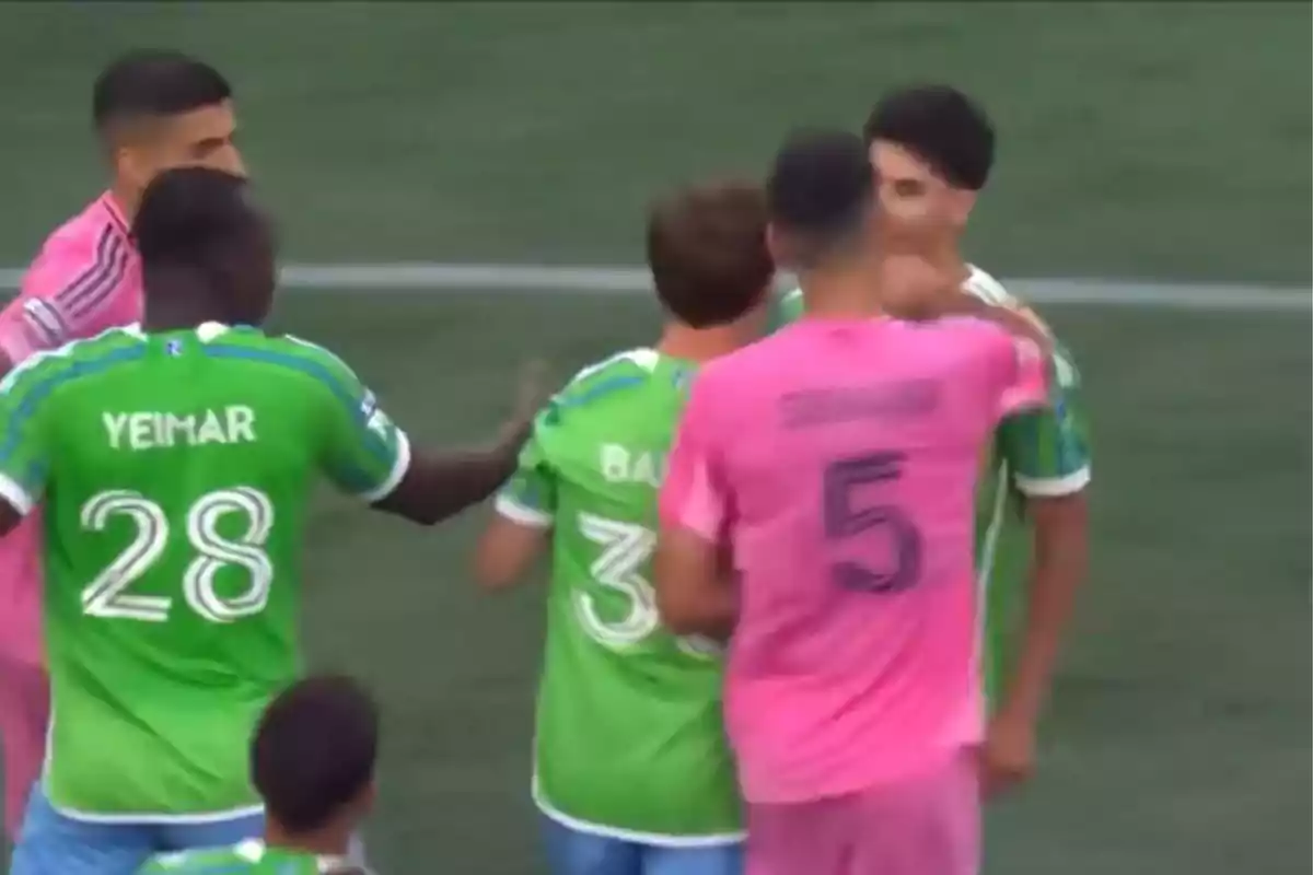 Jugadores de dos equipos de fútbol, uno con uniforme verde y otro con uniforme rosa, discuten en el campo durante un partido. Jugadores de dos equipos de fútbol, uno con uniforme verde y otro con uniforme rosa, discuten en el campo durante un partido.