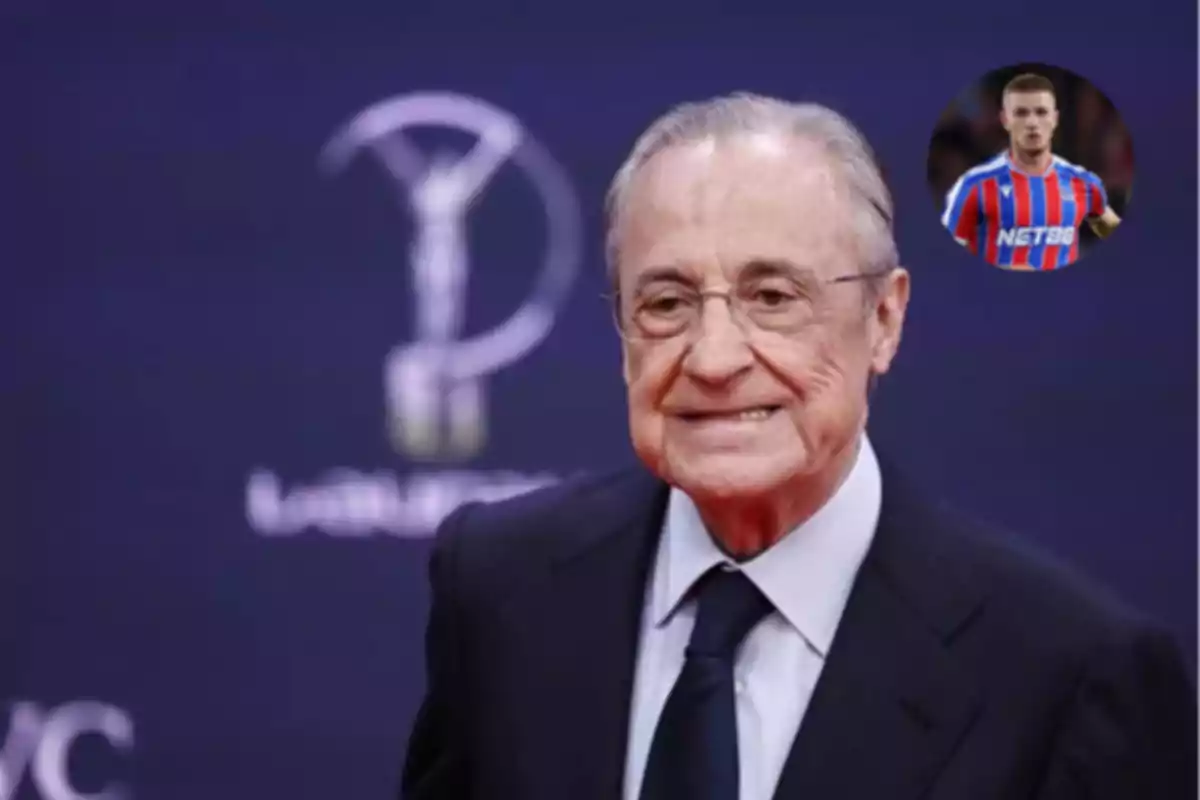 Older man with glasses and a dark suit smiles in front of a blue background with a blurry logo, and in the top right corner there is a box showing a player wearing a red and blue striped uniform.