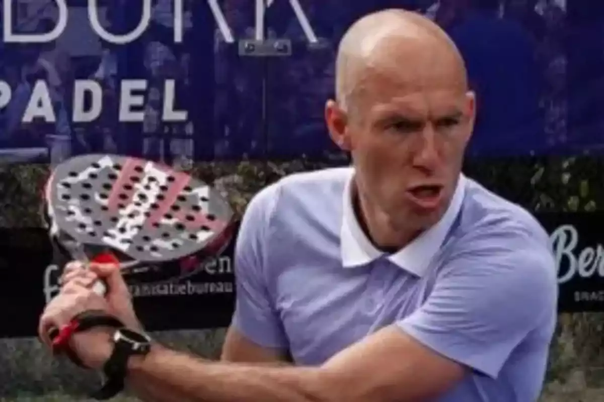 Bald man wearing a purple polo jersey playing padel and holding a racket in a hitting position Bald man wearing a purple polo jersey playing padel and holding a racket in a hitting position