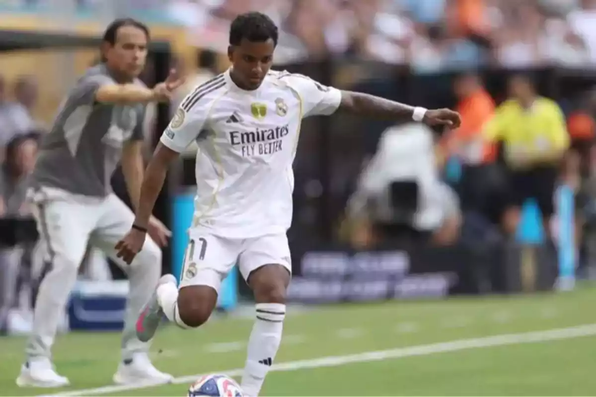Futbolista del Real Madrid a punto de golpear el balón durante un partido con un entrenador dando indicaciones al fondo Futbolista del Real Madrid a punto de golpear el balón durante un partido con un entrenador dando indicaciones al fondo