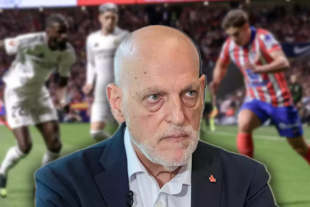 Bald man with a serious expression in the foreground with a blurred soccer match in the background where players from two teams are competing on the field.
