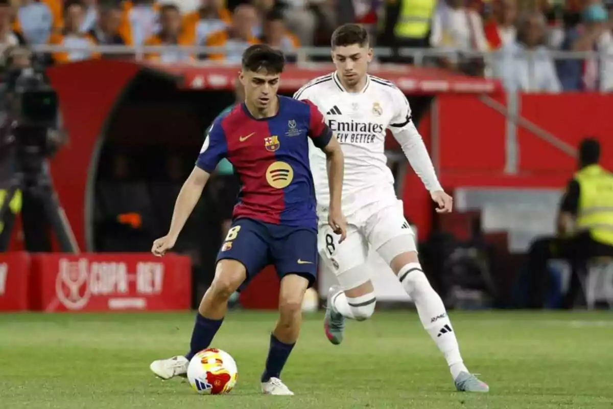 Dos futbolistas de los equipos Barcelona y Real Madrid disputan el balón durante un partido en un estadio lleno de espectadores.