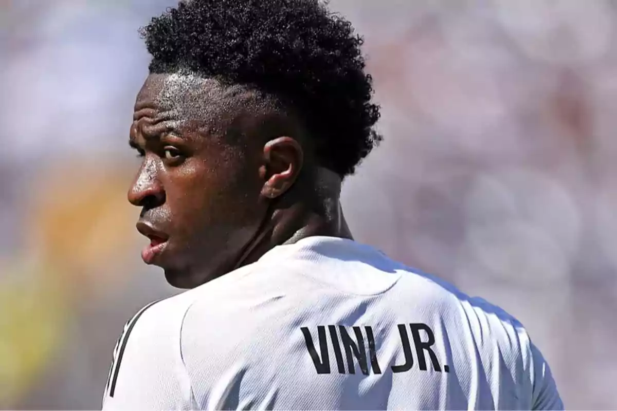Soccer player wearing a white jersey with the name Vini Jr on the back looking to the side during a match Soccer player wearing a white jersey with the name Vini Jr on the back looking to the side during a match