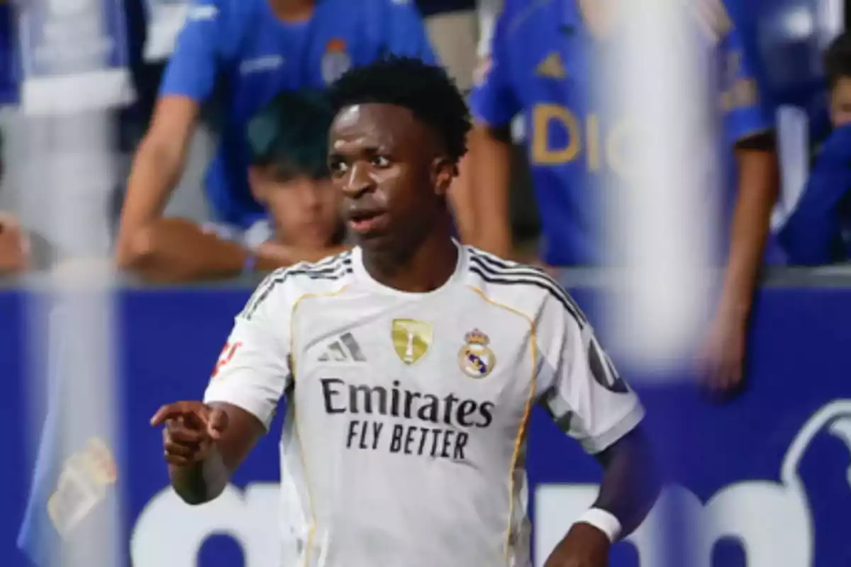 Futbolista del Real Madrid con uniforme blanco durante un partido señalando con la mano y aficionados en las gradas al fondo Futbolista del Real Madrid con uniforme blanco durante un partido señalando con la mano y aficionados en las gradas al fondo