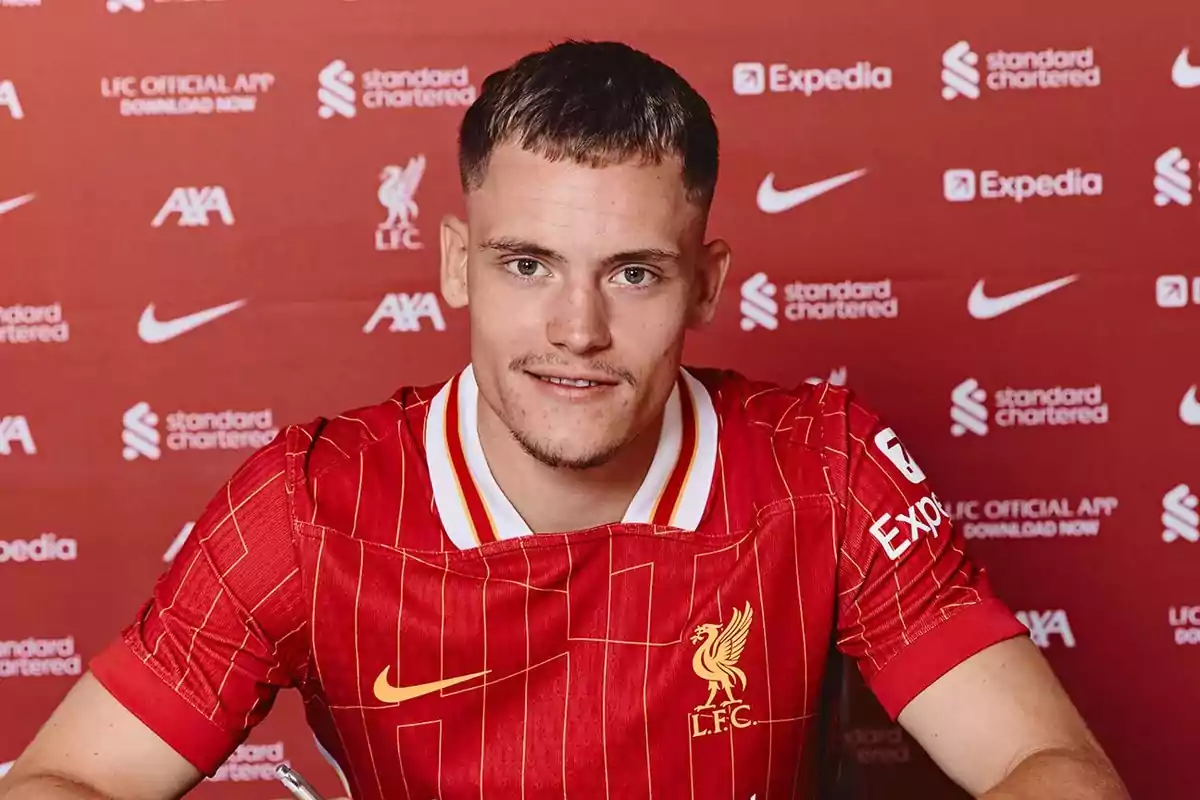 Soccer player wearing a Liverpool jersey posing in front of a backdrop with sponsor logos Soccer player wearing a Liverpool jersey posing in front of a backdrop with sponsor logos