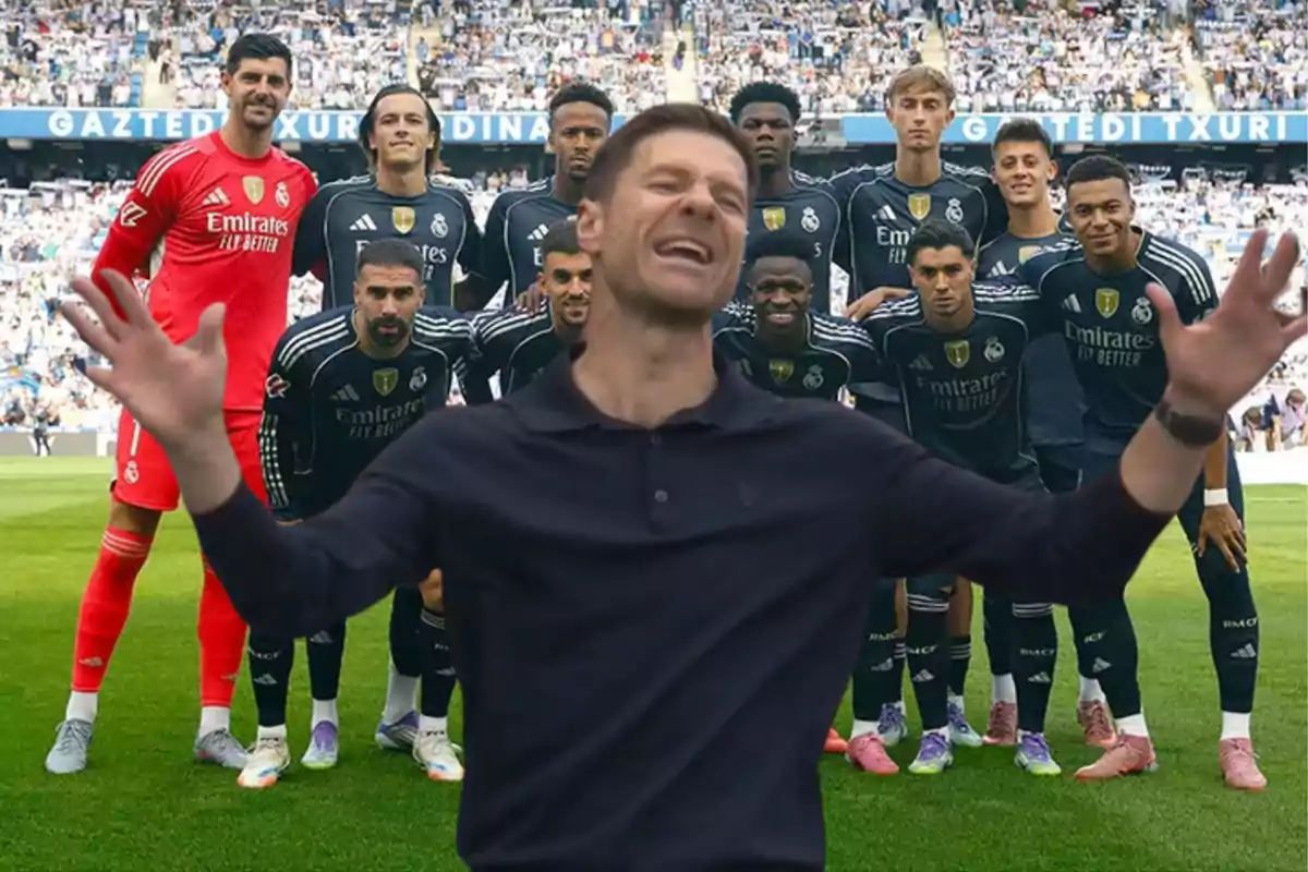 A smiling man with open arms appears in front of a soccer team posing on the field.