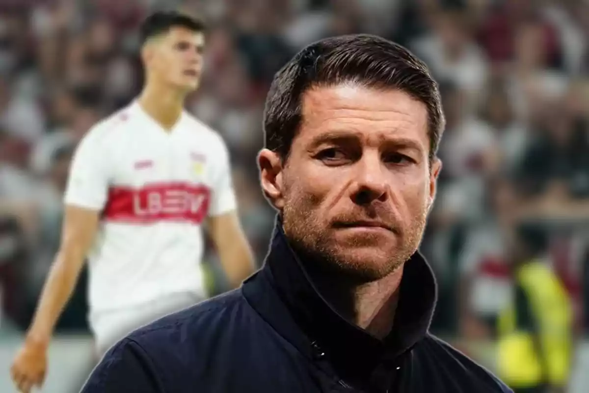 Entrenador de fútbol en primer plano con expresión seria y jugador desenfocado al fondo en un estadio lleno de público