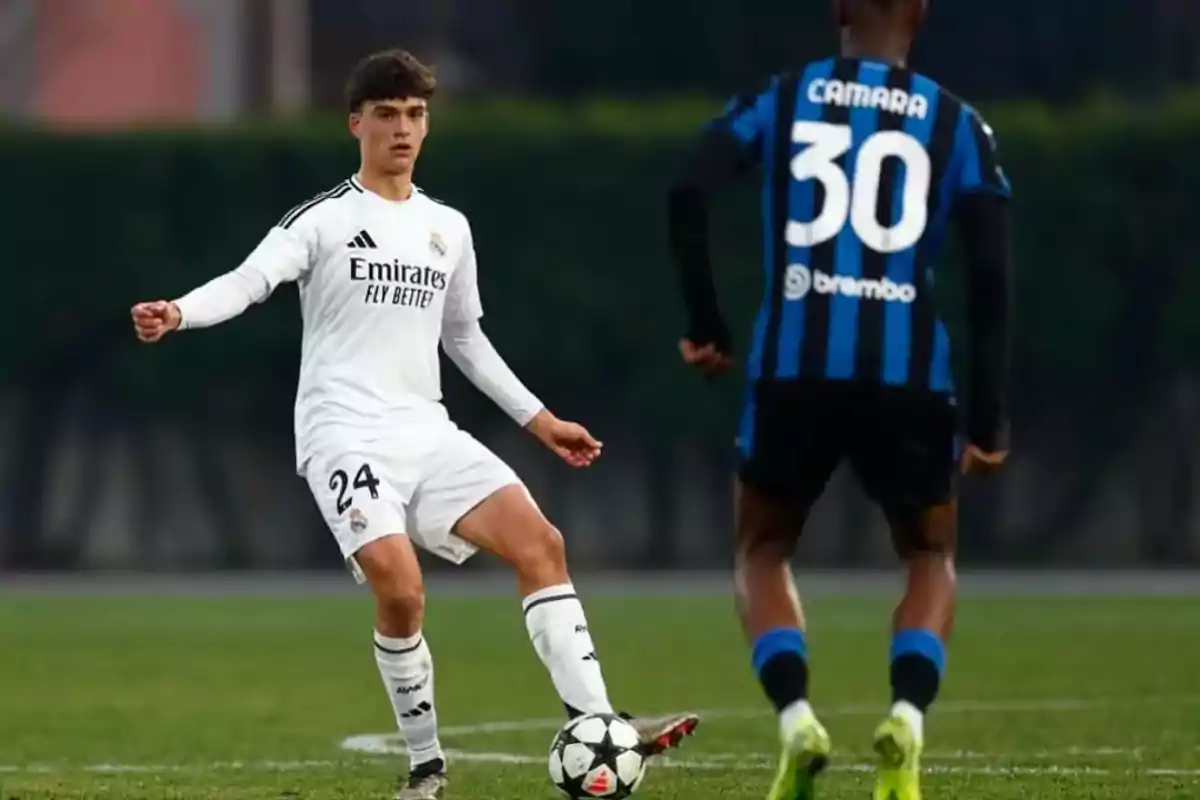 A Real Madrid player controls the ball while an opponent from the team in blue and black uniform faces him in a soccer match. A Real Madrid player controls the ball while an opponent from the team in blue and black uniform faces him in a soccer match.