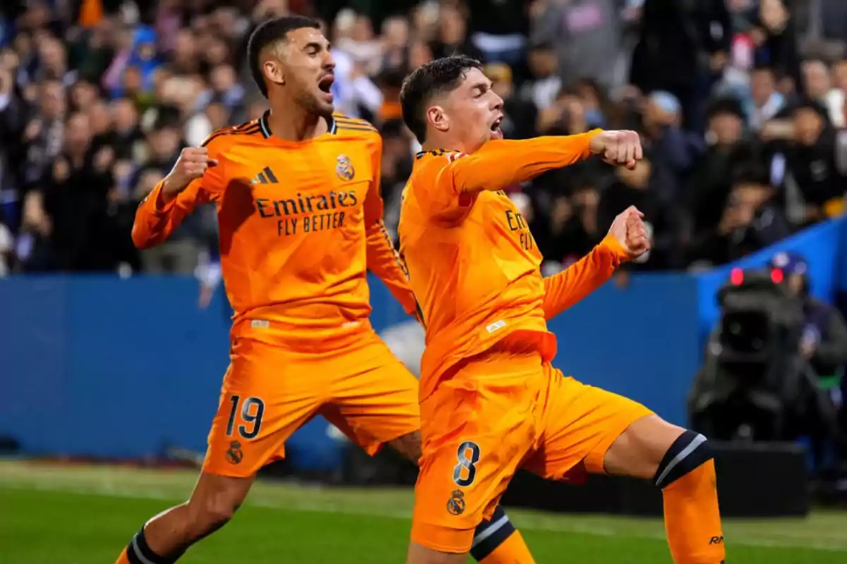 Football players celebrating a goal in a match in orange uniforms.