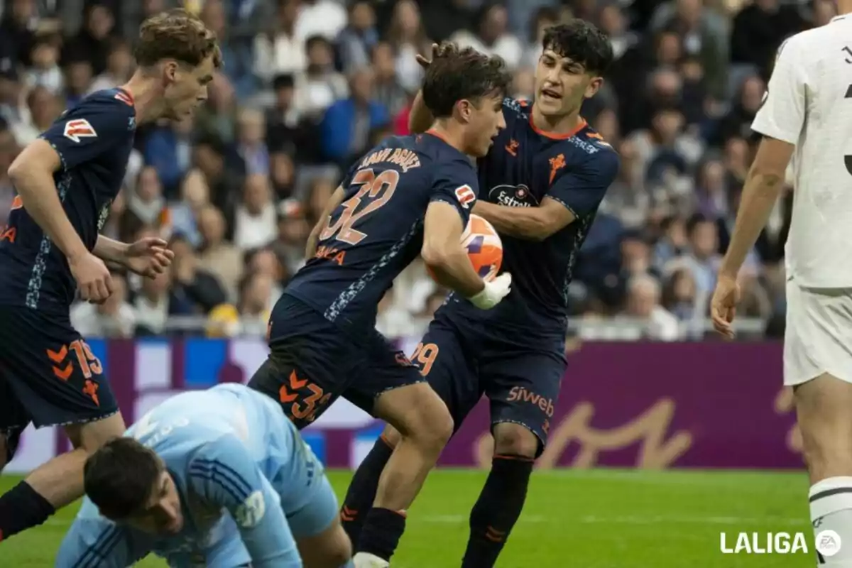 Soccer players in action during a match, one of them holding the ball while another cheers him on, with a goalkeeper on the ground and an opposing team player nearby. Soccer players in action during a match, one of them holding the ball while another cheers him on, with a goalkeeper on the ground and an opposing team player nearby.