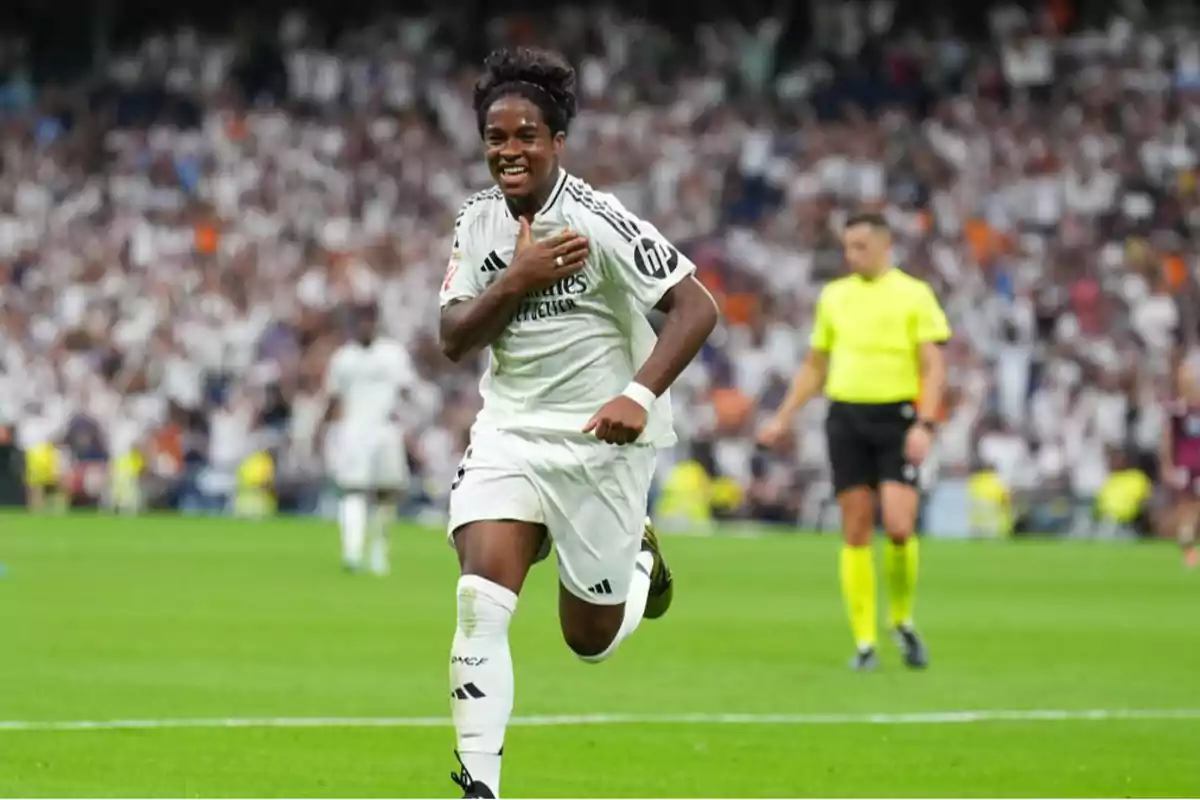 Un jugador de fútbol sonríe mientras corre en el campo durante un partido con el uniforme blanco del equipo.