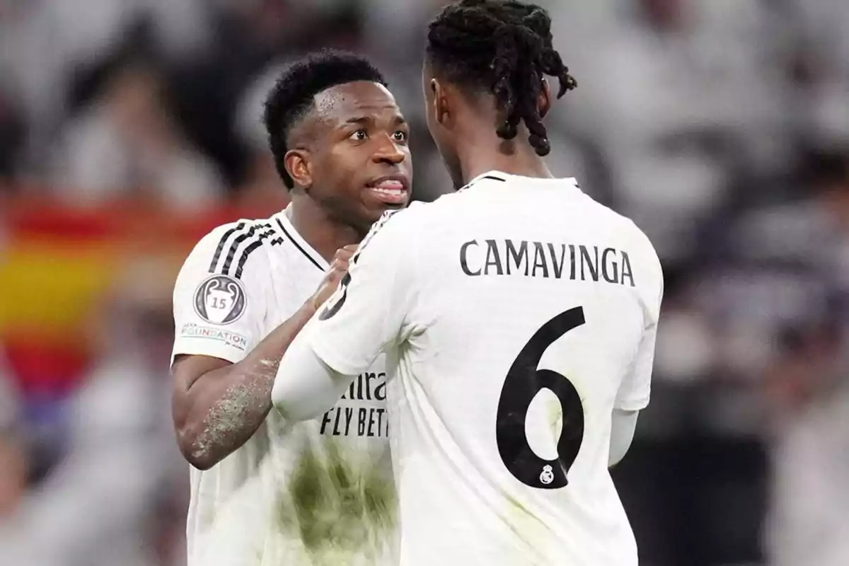 Two players in white uniforms talk on the field during a match.