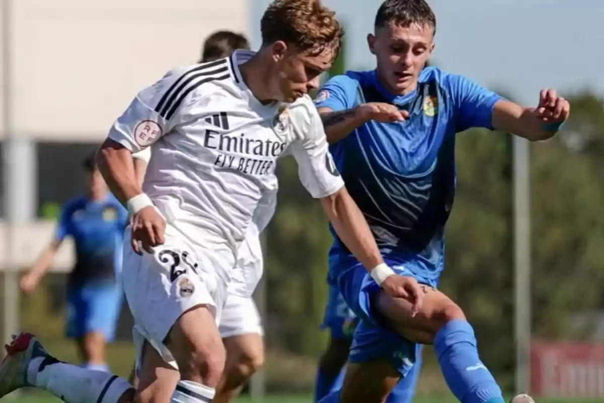 Two soccer players compete for the ball in a match, one dressed in white and the other in blue. Two soccer players compete for the ball in a match, one dressed in white and the other in blue.