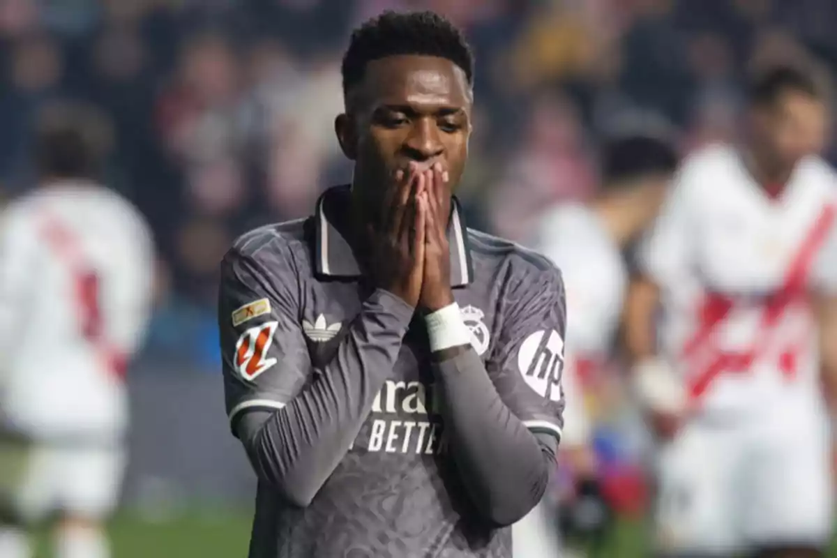 Un jugador de fútbol con uniforme gris se lleva las manos al rostro en un gesto de frustración durante un partido.