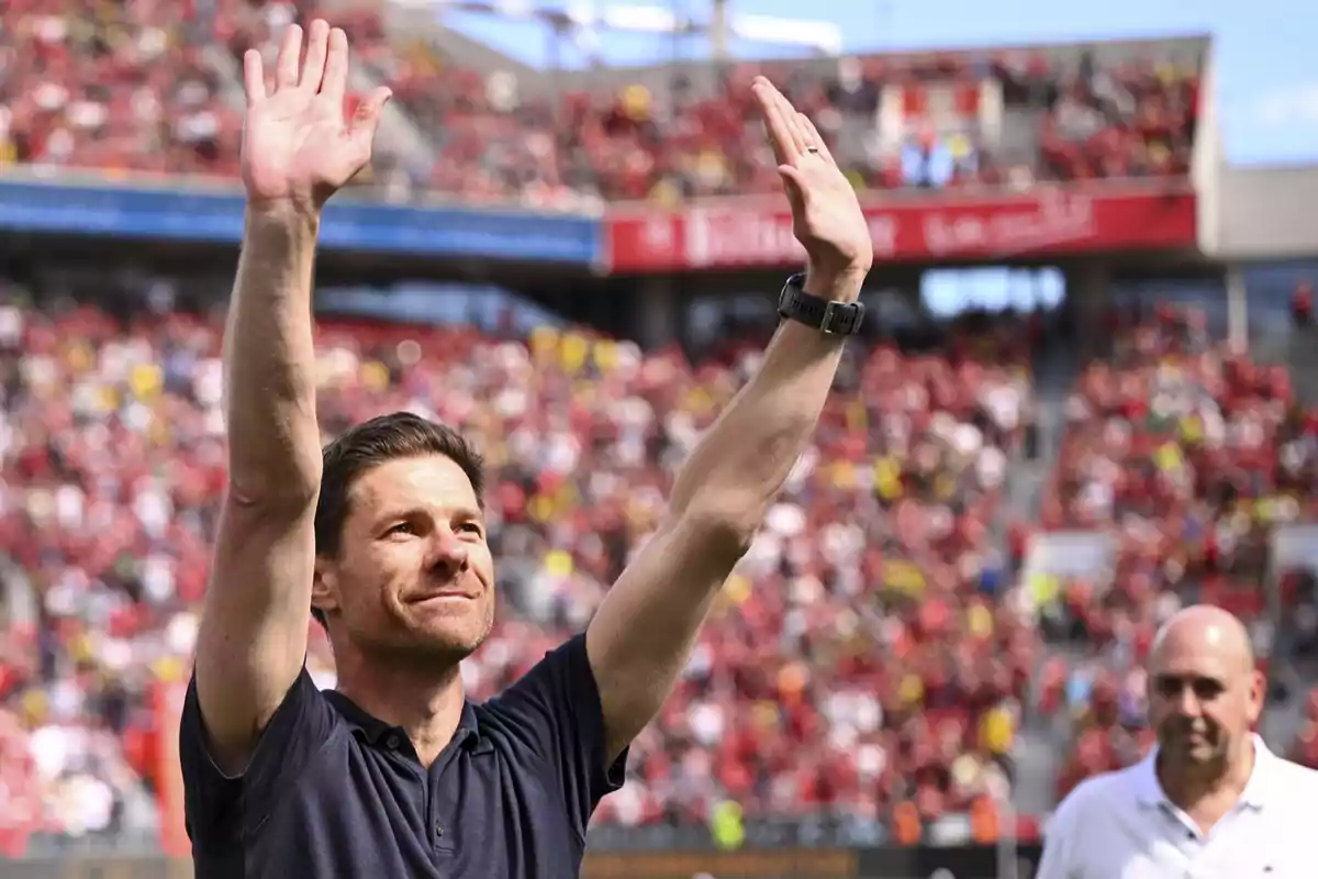 A man in a dark jersey raises his hands in a stadium full of spectators.
