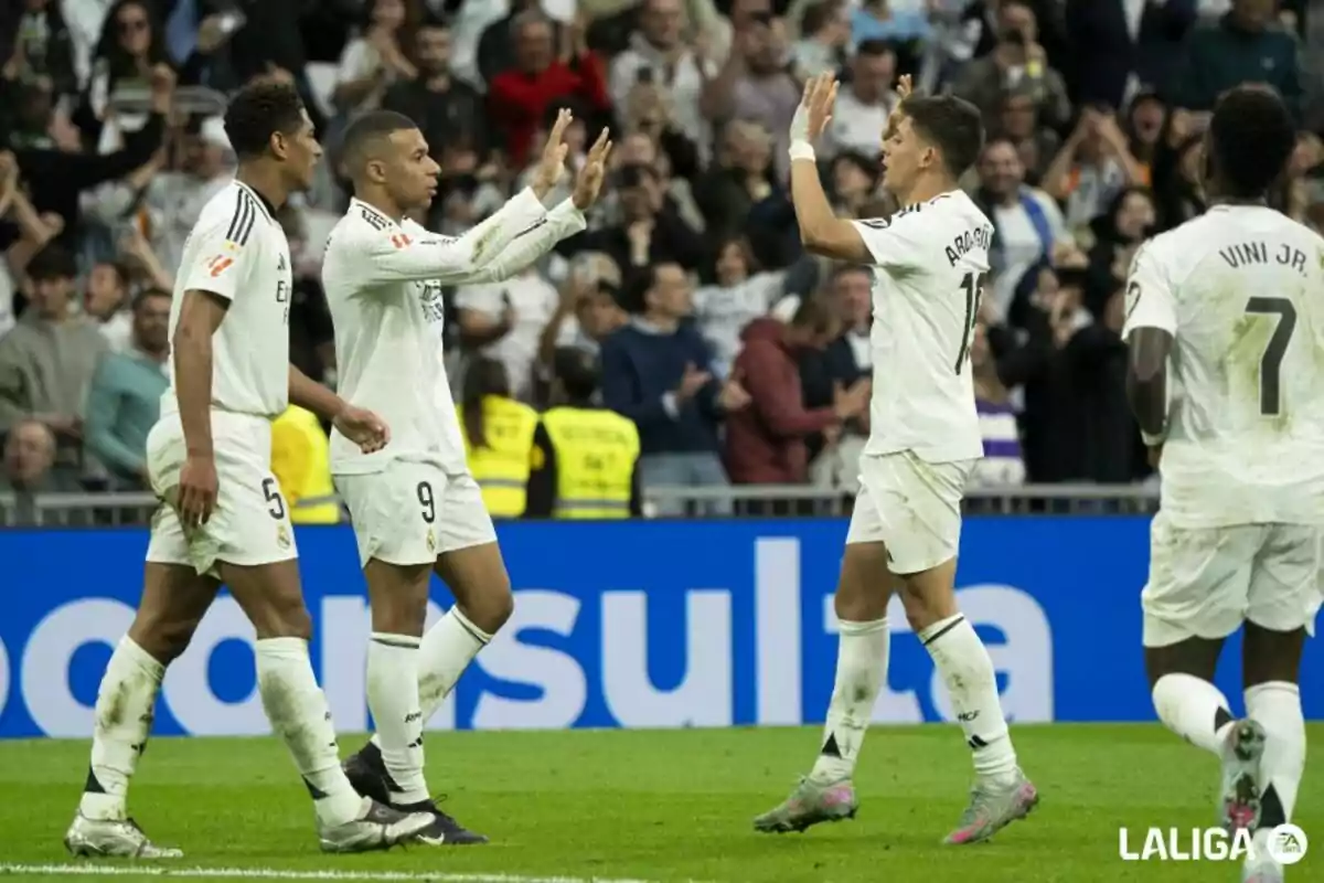 Soccer players celebrating a goal on the field with the crowd applauding in the background.