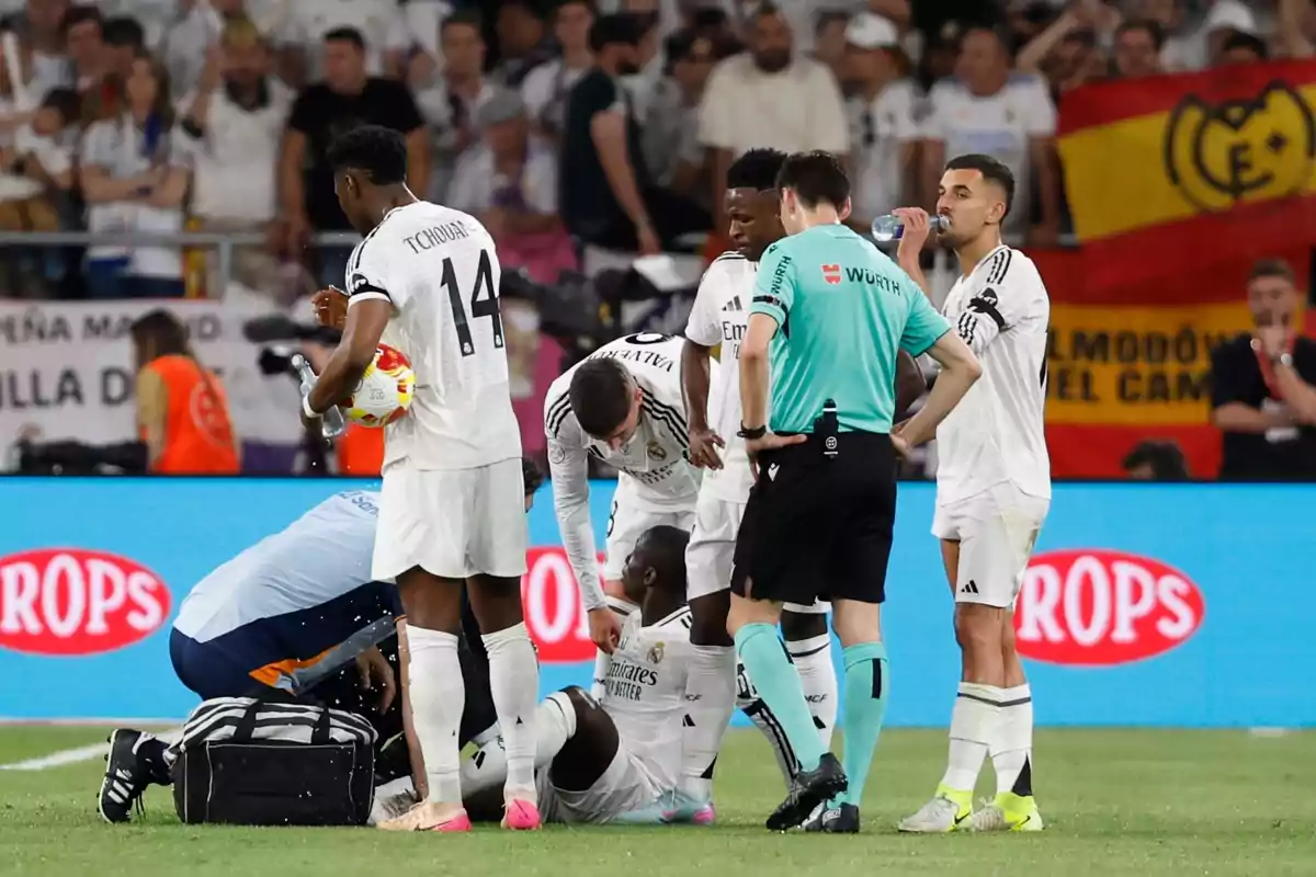 Soccer players and a referee surround an injured teammate on the field while a doctor attends to him. Soccer players and a referee surround an injured teammate on the field while a doctor attends to him.