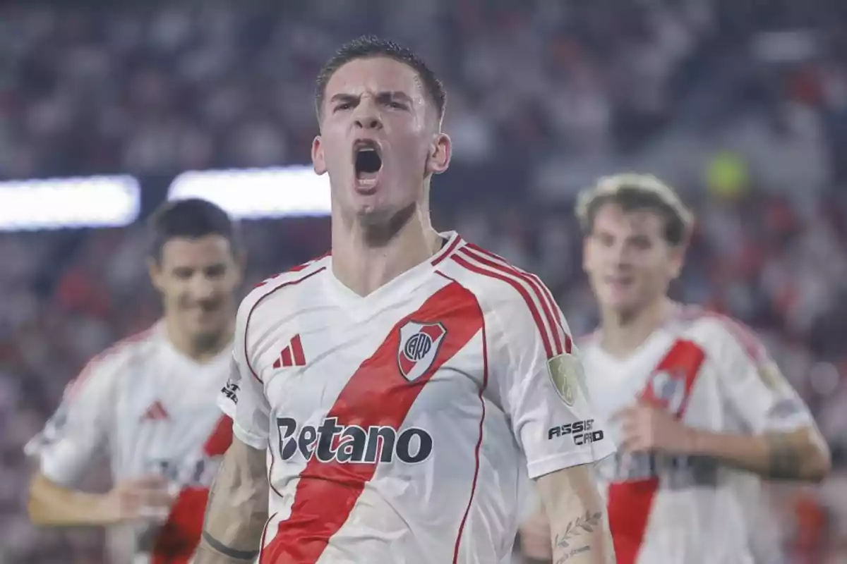 A player wearing the River Plate jersey celebrates effusively on the field while other players are seen in the background. A player wearing the River Plate jersey celebrates effusively on the field while other players are seen in the background.