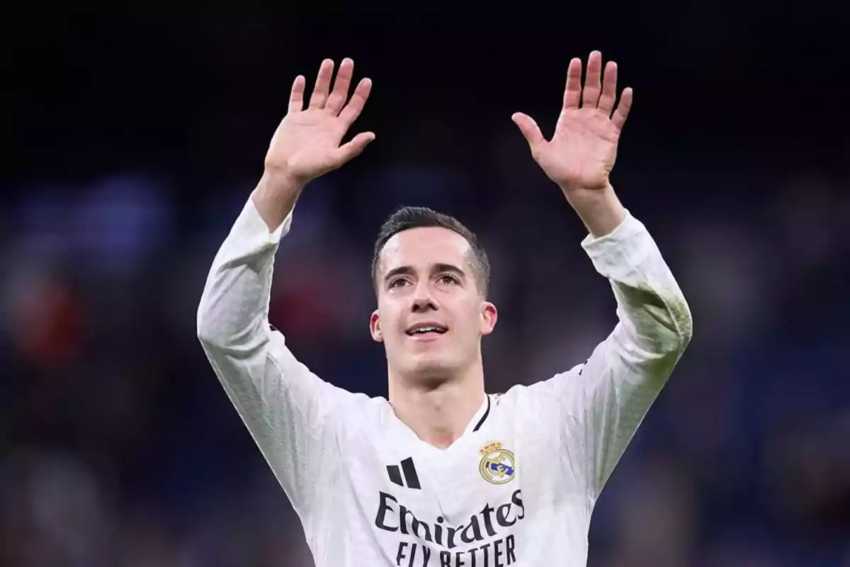 Un jugador de fútbol con uniforme blanco levanta las manos en señal de saludo o celebración.