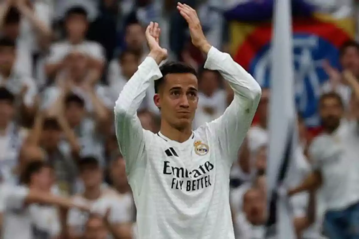 Un jugador de fútbol aplaude en el campo mientras lleva una camiseta blanca, con una multitud de personas al fondo.