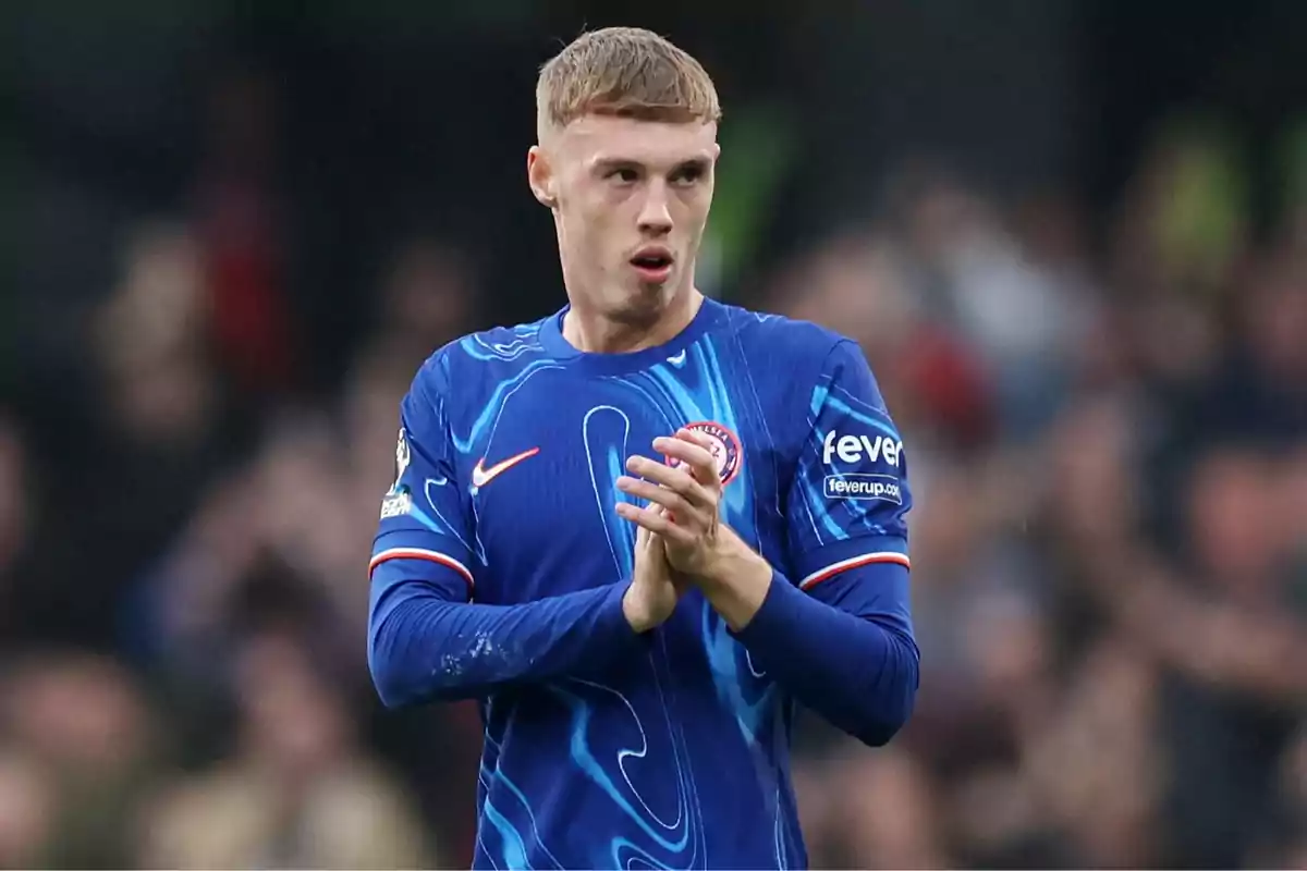 A soccer player in a blue uniform applauds on the field during a match.