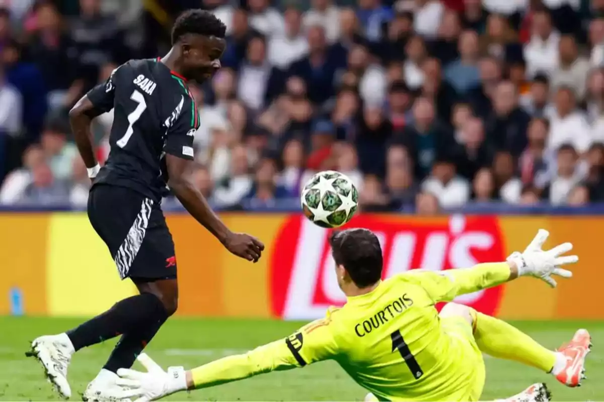 Un jugador de fútbol con uniforme negro intenta anotar mientras el portero, vestido de amarillo, se lanza para detener el balón en un partido. Un jugador de fútbol con uniforme negro intenta anotar mientras el portero, vestido de amarillo, se lanza para detener el balón en un partido.