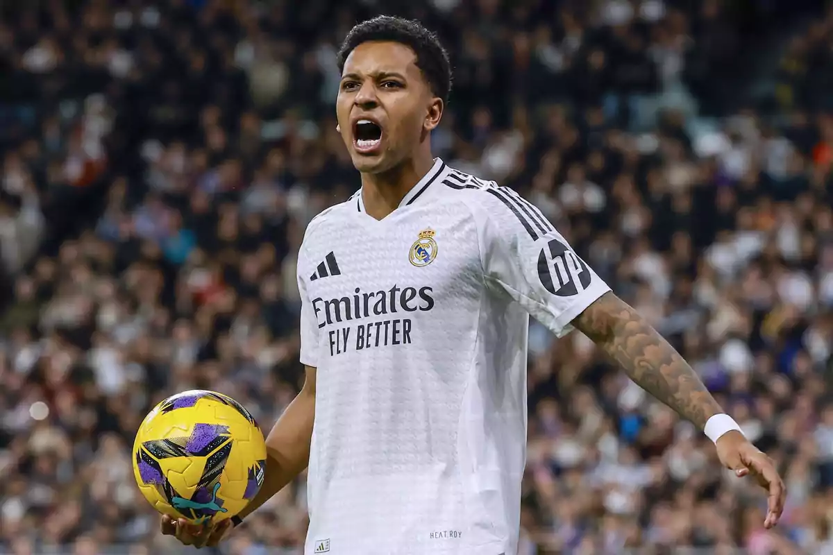 A player in a white uniform holds a yellow ball in a stadium full of spectators.