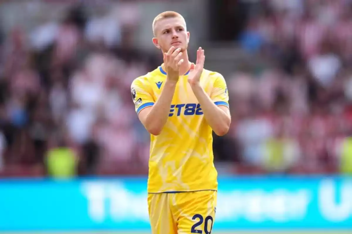 A player in a yellow uniform applauds in a stadium. A player in a yellow uniform applauds in a stadium.