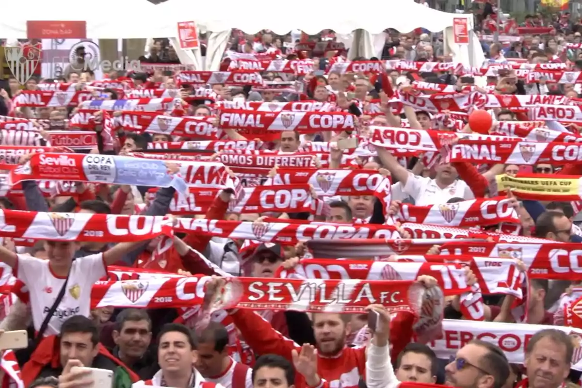 Aficionados del Sevilla FC celebran levantando bufandas rojas y blancas en un evento deportivo. Aficionados del Sevilla FC celebran levantando bufandas rojas y blancas en un evento deportivo.