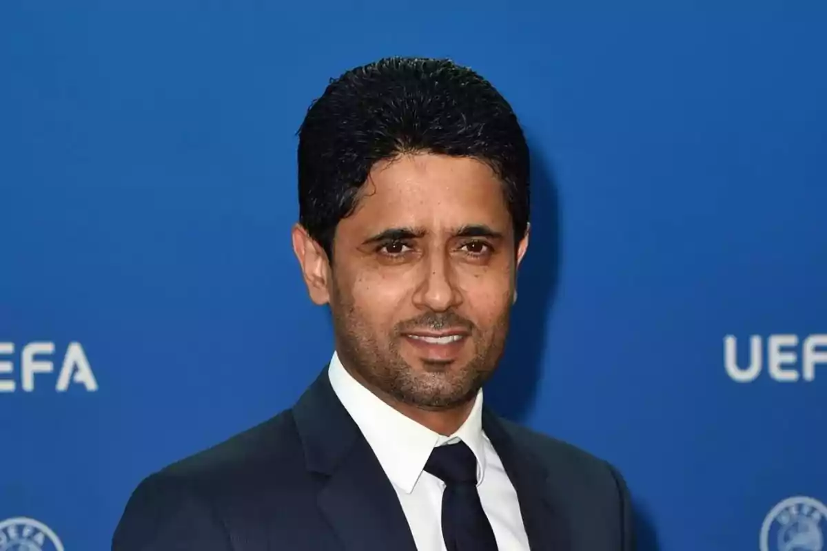 Man in a dark suit and tie posing in front of a blue background with the UEFA logo